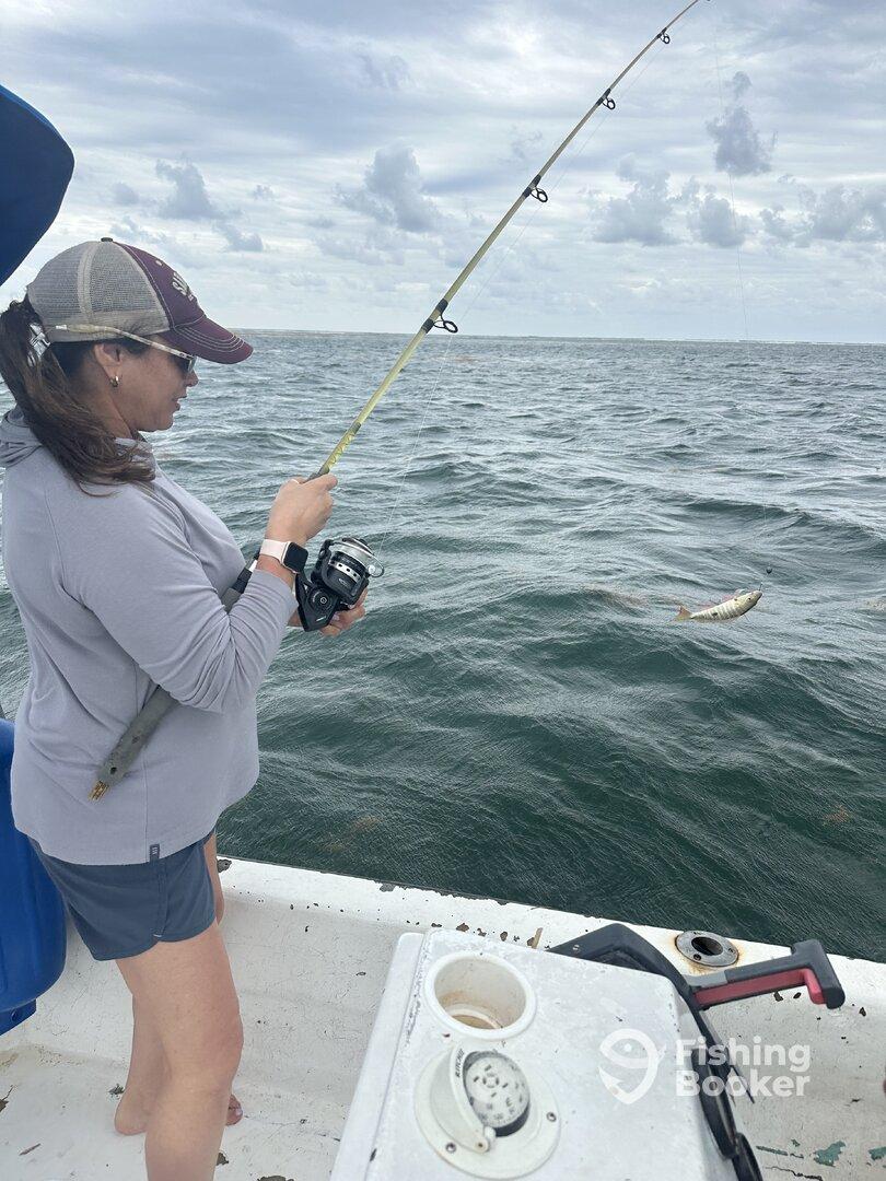 A female angler is actively reeling in a fish while fishing on a boat, showcasing the excitement of the catch in a coastal environment.