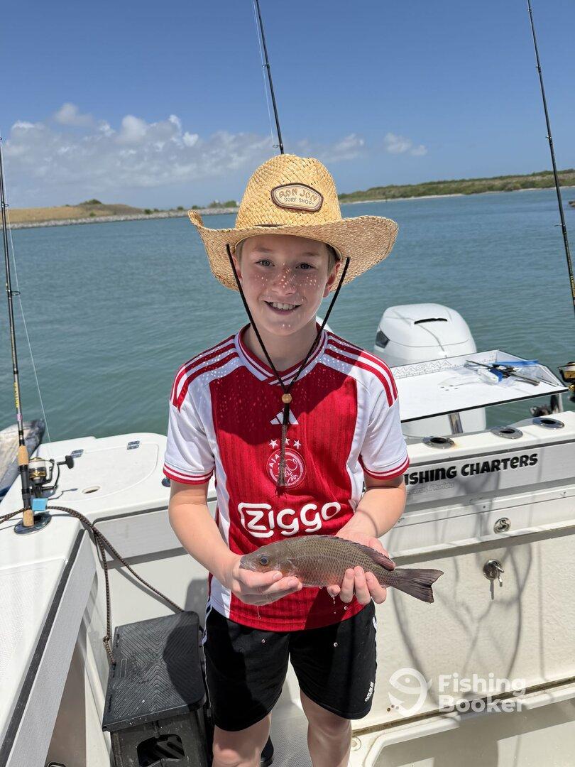 A young angler proudly displaying a freshly caught fish aboard a fishing charter, enjoying a sunny day on the water.
