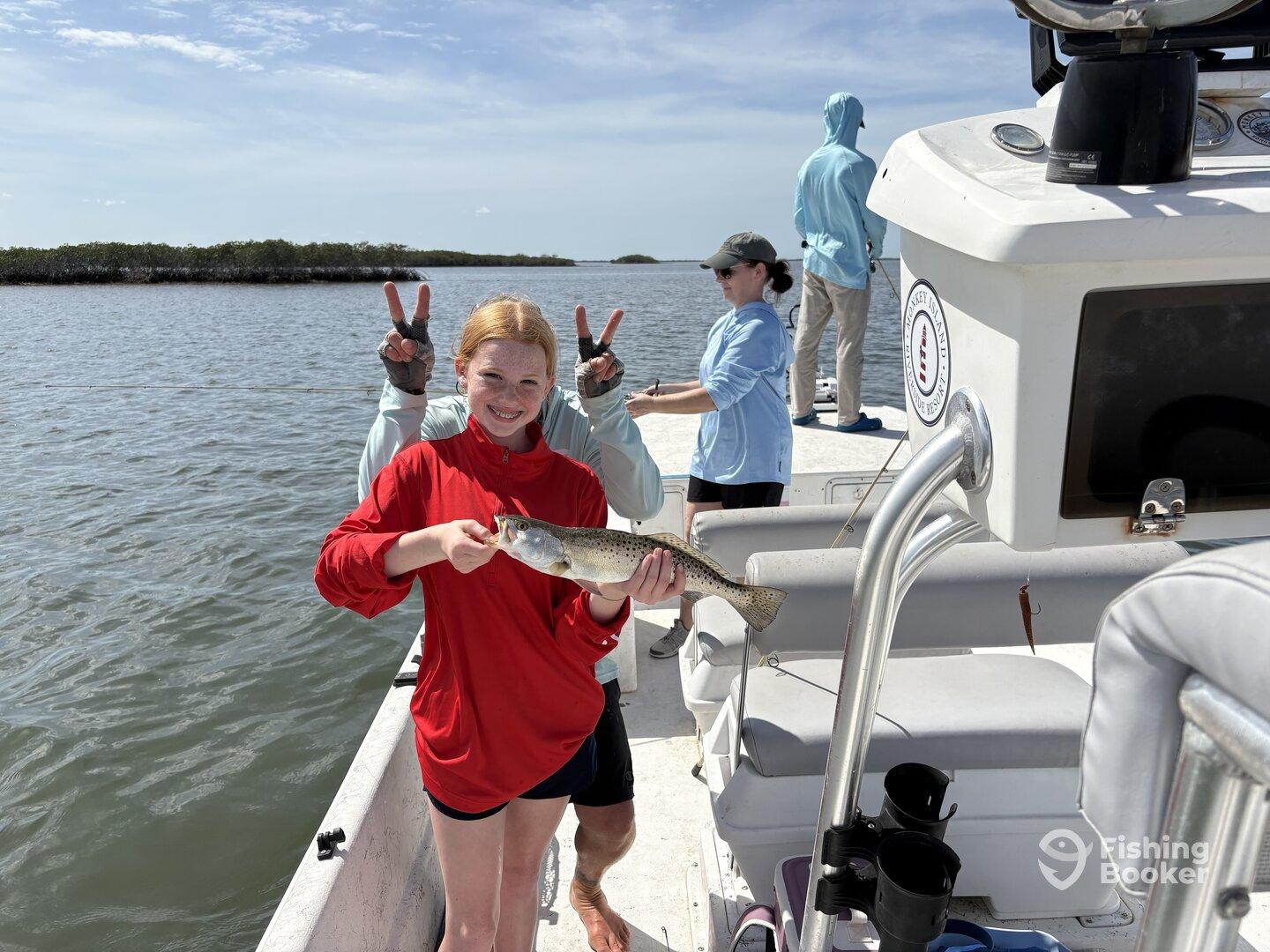A young angler proudly displaying a Speckled Trout while fishing with family on a sunny day in a coastal waterway.