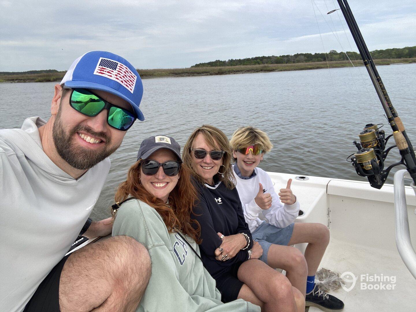 A family enjoying a day on the water, posing together on a fishing boat with fishing gear visible in the background.