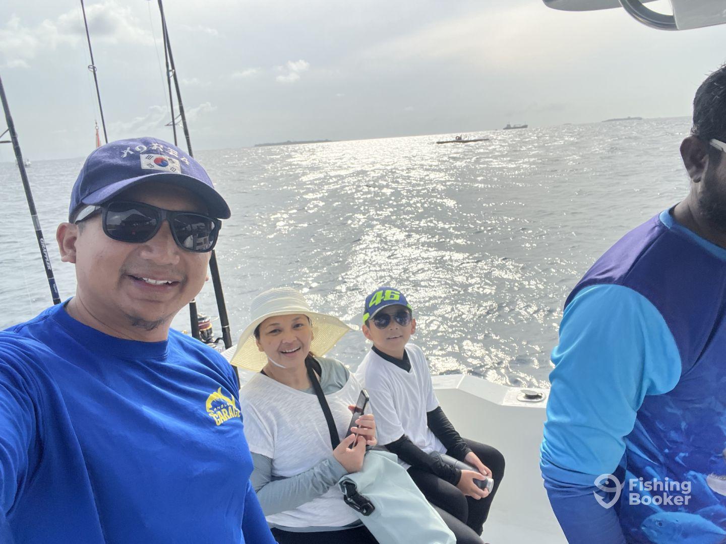 A family enjoying a fishing trip aboard a boat, with a scenic view of the water in the background.