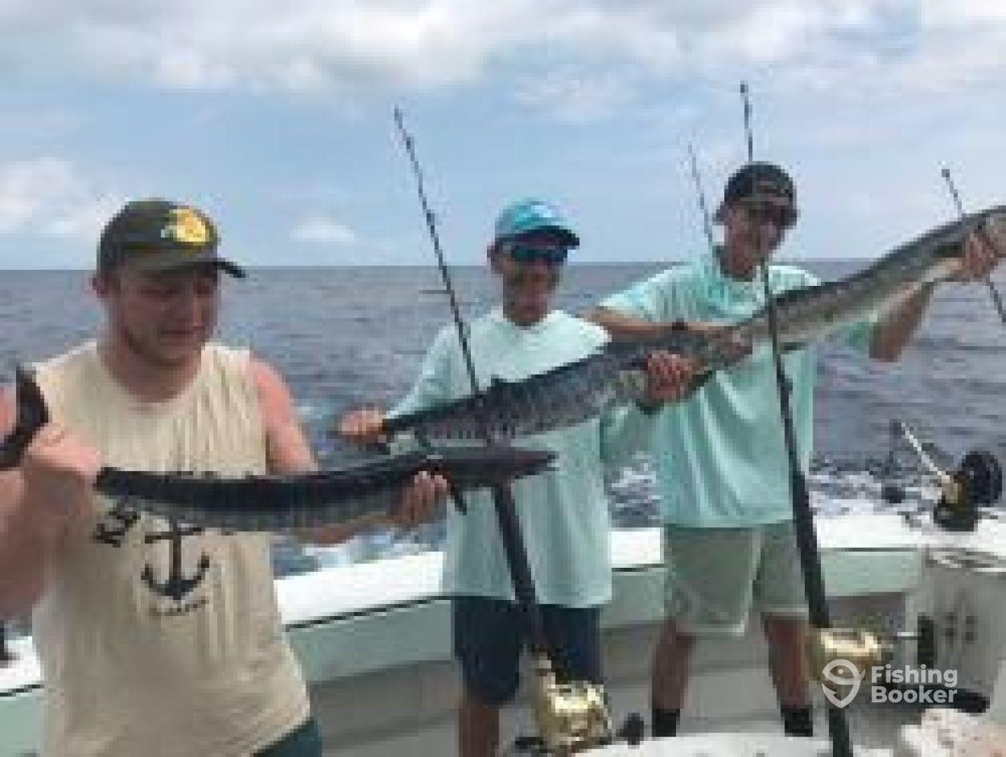 Three anglers proudly displaying their catch of Barracuda while fishing offshore, showcasing a successful day on the water.