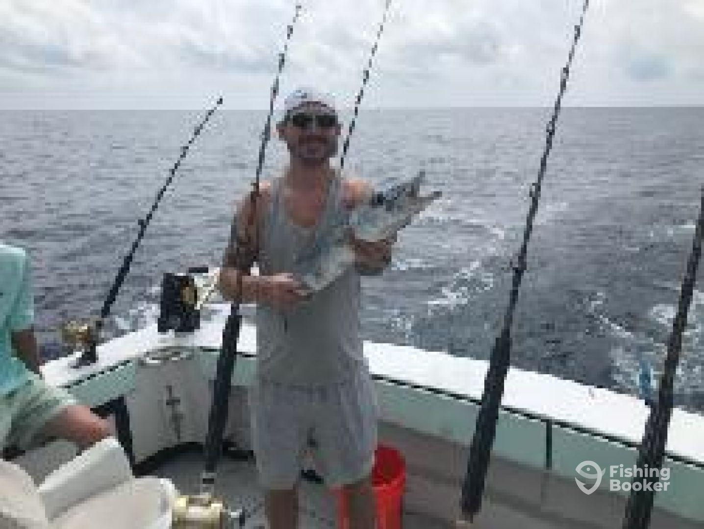 Angler proudly displaying a caught fish aboard a fishing boat in open waters, showcasing the excitement of a successful fishing trip.