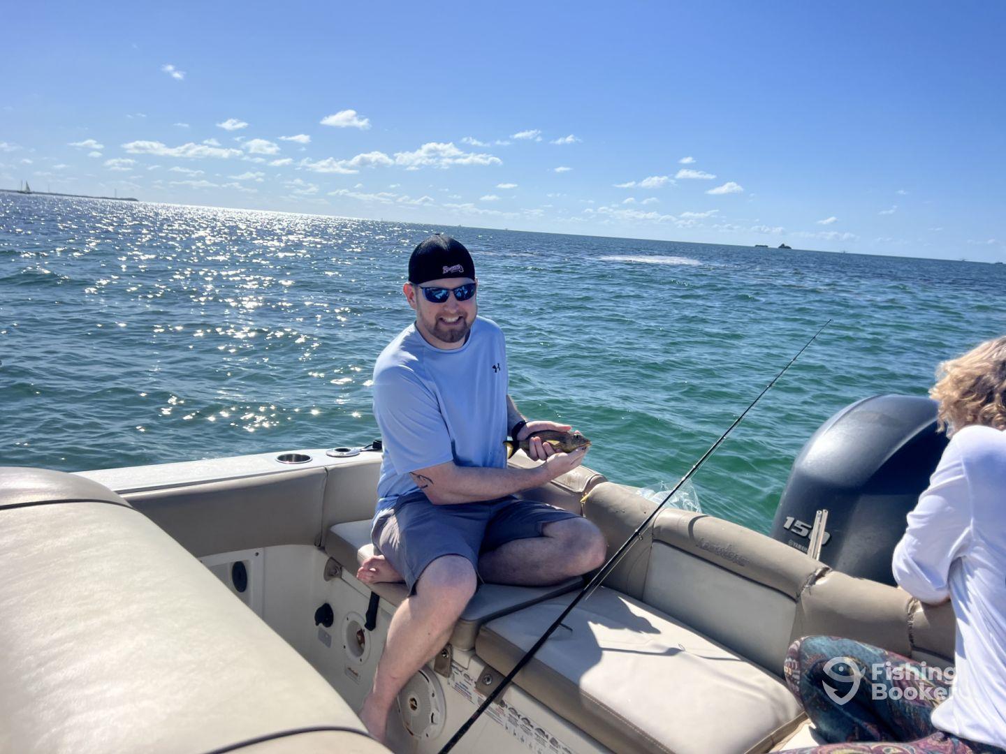 An angler proudly displaying a catch while seated on a boat, enjoying a sunny day on the water.