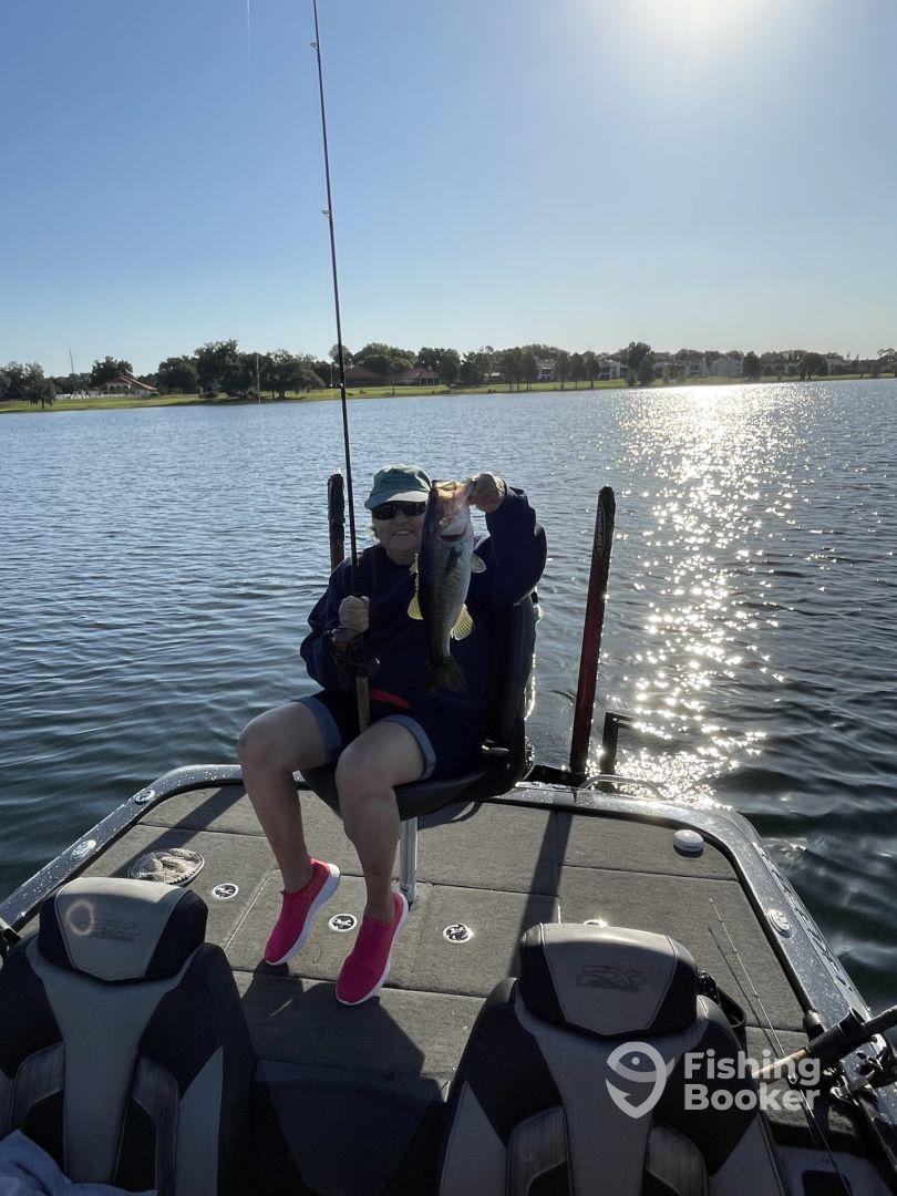An angler proudly displaying a large Largemouth Bass while seated on a fishing boat, enjoying a sunny day on the water.