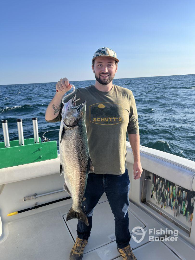 An angler proudly displaying a large Salmon aboard a fishing boat, with a scenic ocean backdrop.