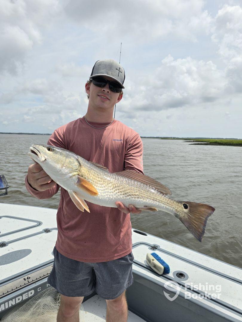 Young angler proudly holding a large Redfish while fishing in a scenic coastal environment.