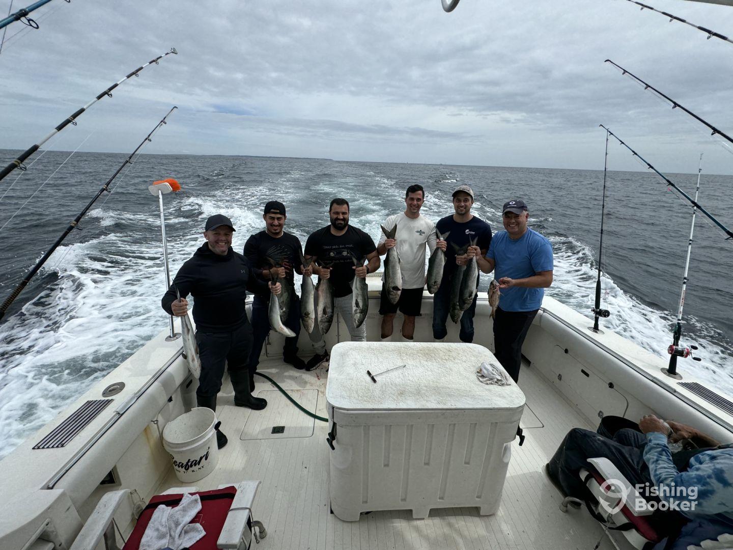 Group of anglers proudly displaying their catch of several fish while aboard a sport fishing boat in open waters.