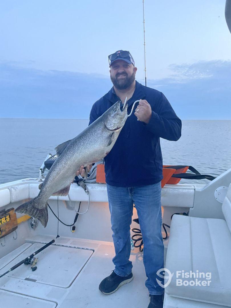 An angler proudly displaying a large Lake Trout aboard a fishing boat during a serene evening on the water.
