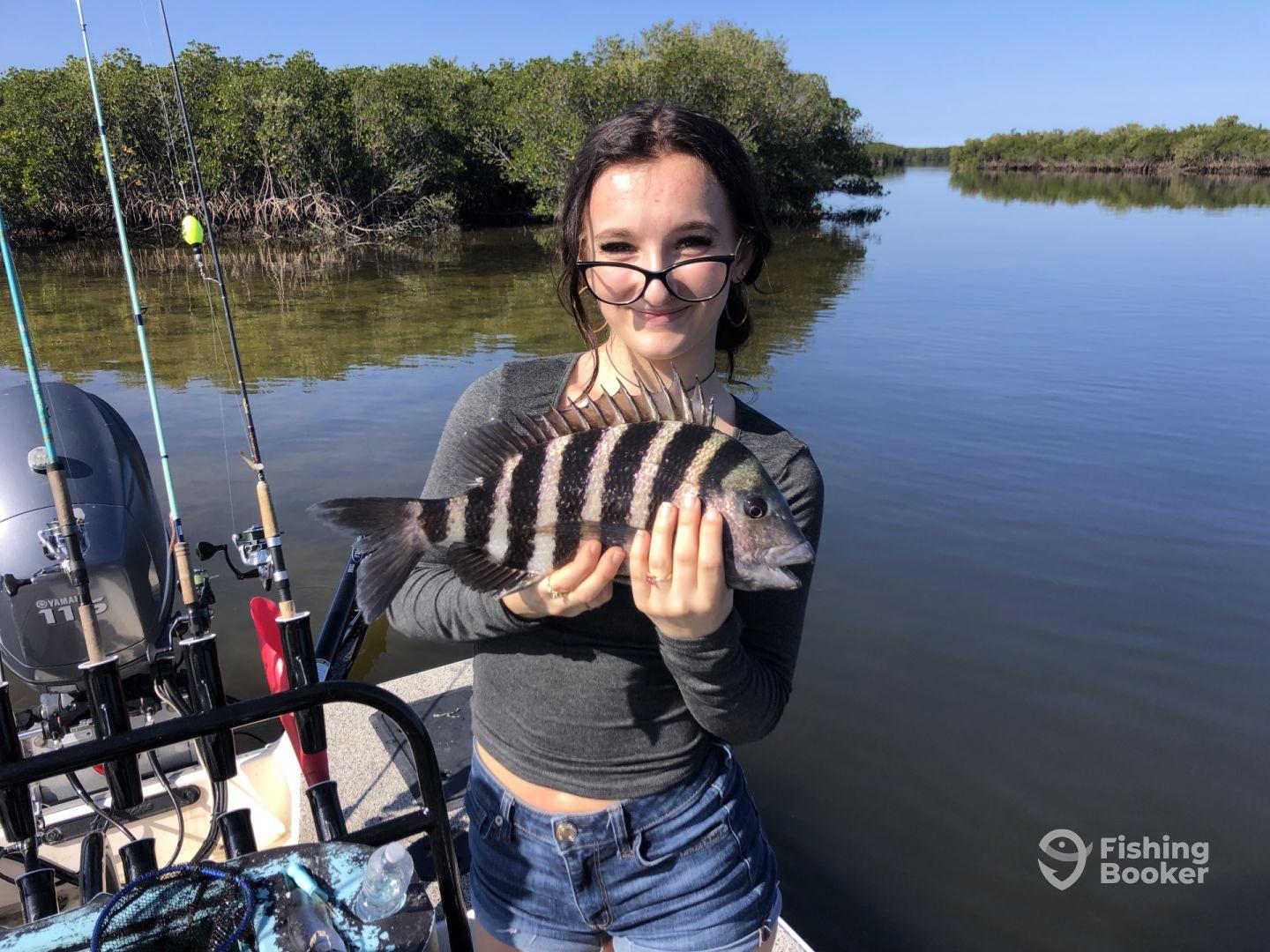 A young angler proudly displaying a Sheepshead caught while fishing in a scenic mangrove area.