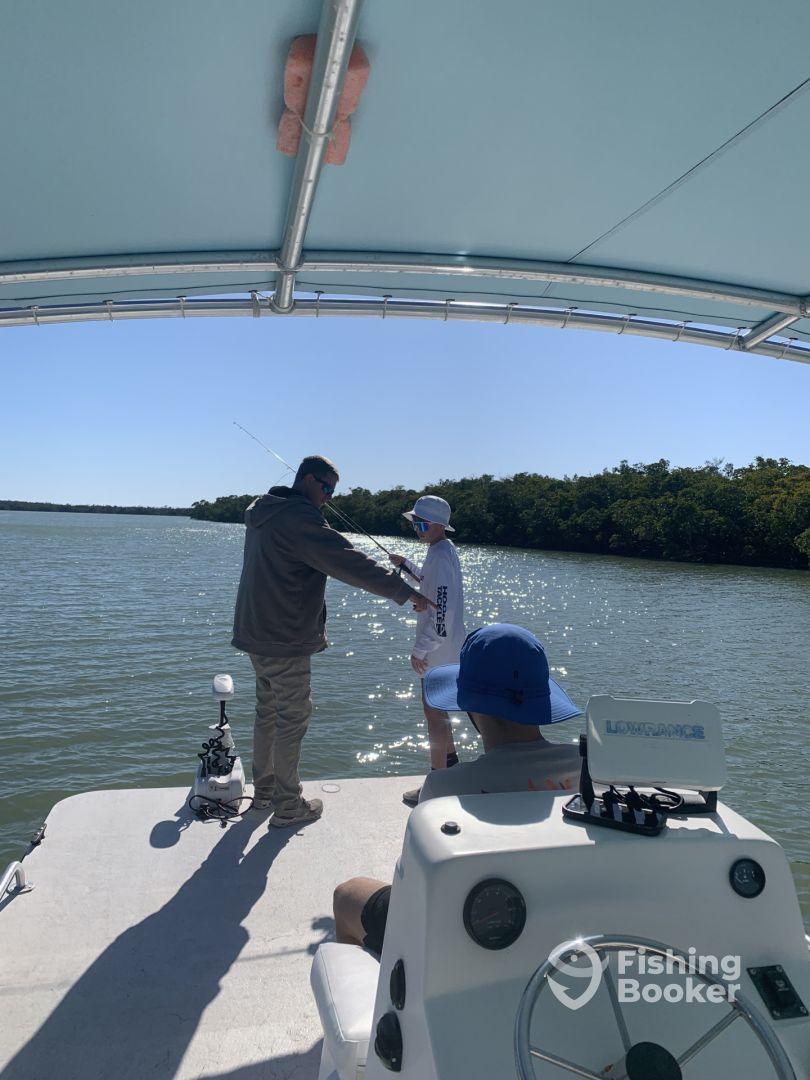 Two anglers engaged in fishing on a boat in a scenic waterway, with one person instructing a young angler.