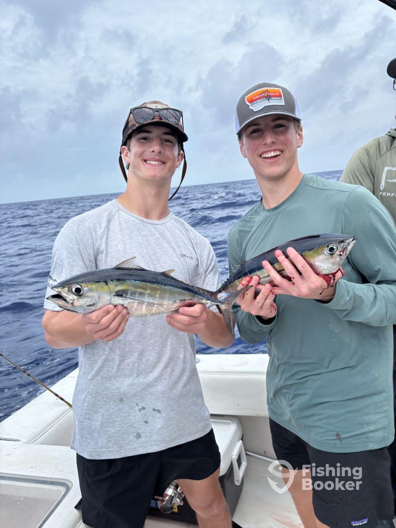 Two young anglers proudly displaying their catch of Mahi Mahi while fishing on a boat in open waters.